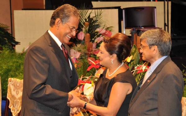 Prime Minister Kamla Persad-Bissessar congratulates Dr. Austin Trinidade who got the Public Service Medal of Merit (Gold). Looking on is Dr. Gregory Bissessar, husband of the Prime Minister